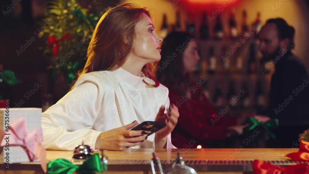 Young elegant woman sitting on bar, looking on phone and waiting for friends or boyfriend to come. Lonely date. Concept of party, winter holidays, celebration, friendship, fun, relaxation Young elegant woman sitting on bar, looking on phone and waiting for friends or boyfriend to come. Lonely date. Concept of party, winter holidays, celebration, friendship, fun, relaxation