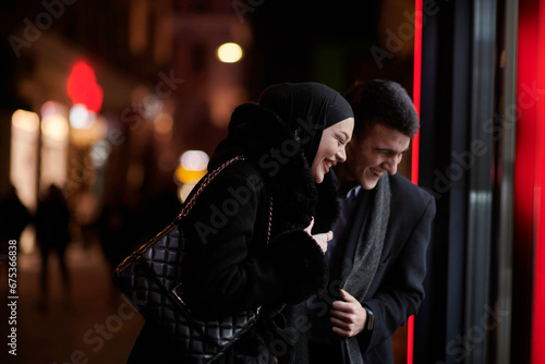 Happy multicultural business couple walking together outdoors in an urban city street at night near a jewelry shopping store window. © .shock