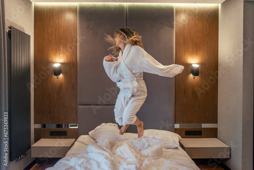 Woman having fun and jumping with bathrobe on bed in hotel room photo