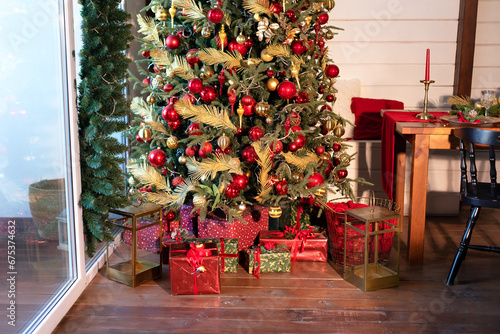 Festive living room interior with decorated Christmas tree and many gifts. Xmas tree with lights glowing garlands at evening. Christmas at home. New year winter home decor.