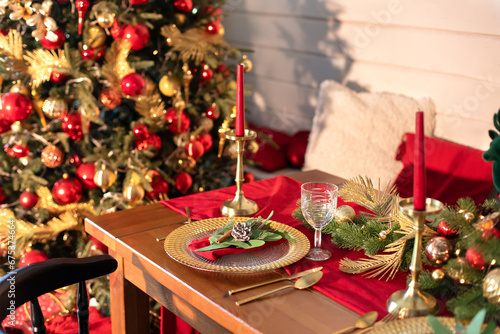Festive table setting for Christmas dinner at home. Holiday Served table with decorations  candles and garland. Beautiful table setting with Christmas decorations and dishware in living room. 