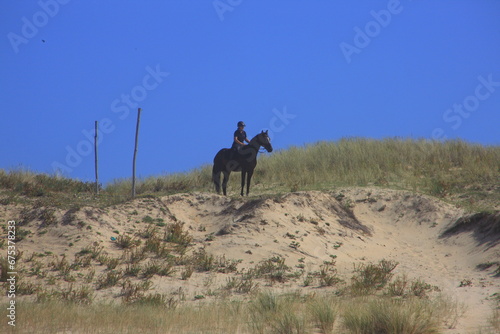 Rider stands with his horse on top of a dune © JorGillwald