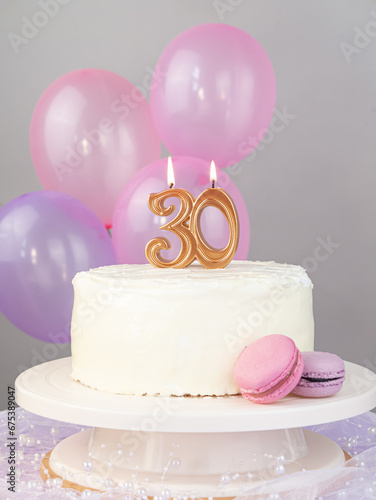 Still life: a lit candle with the number 30 on a white cake with macaroni cakes and pink balls with a place for text, birthday