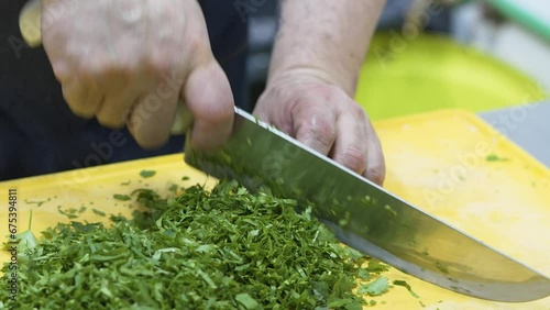 Closeup of a chef cutting the fresh green corianders on the yellow kitchen board with a sharp knife photo