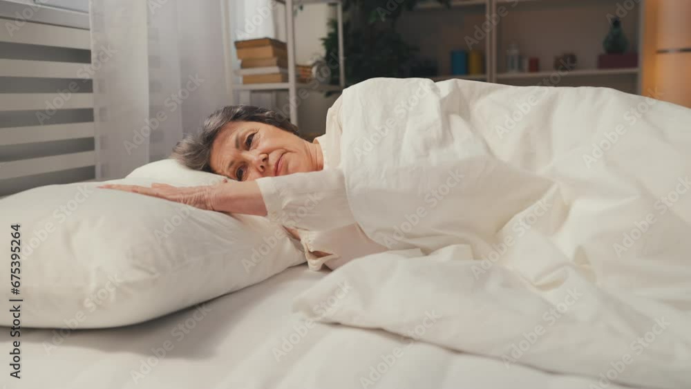 Lonely woman in her 70s lying in bed and touching pillow, missing husband, grief Lonely woman in her 70s lying in bed and touching pillow, missing husband, grief