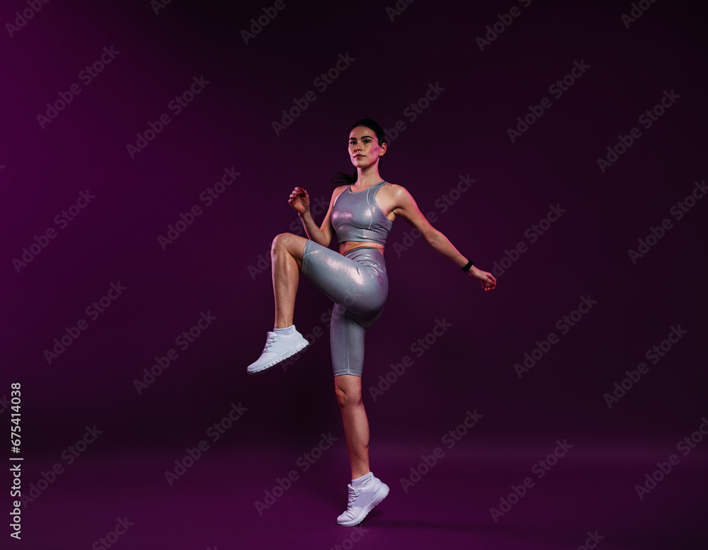 Full length of young slim female in silver sportswear warming up on magenta backdrop Full length of young slim female in silver sportswear warming up on magenta backdrop