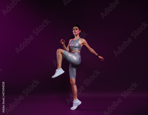 Full length of young slim female in silver sportswear warming up on magenta backdrop