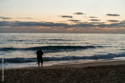 Adult male figure is walking on a sandy beach, gazing out at the sea.