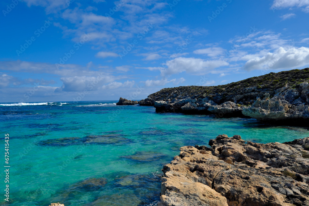 Scenic view of a rocky coastline in the ocean against a bright blue sky