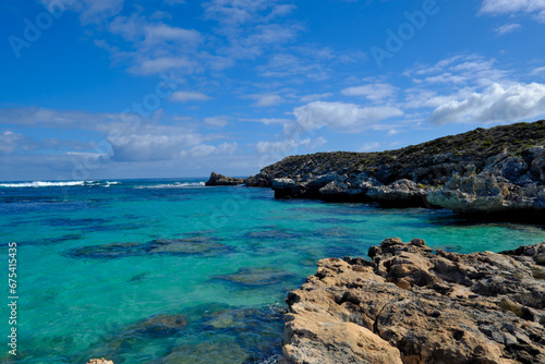 Scenic view of a rocky coastline in the ocean against a bright blue sky