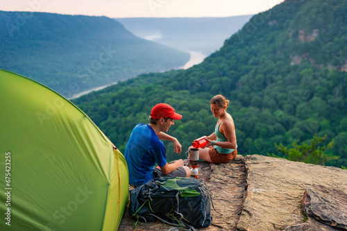 A young man and woman sit outside their tent at a clifftop campsite overlooking a river gorge in Tennessee photo