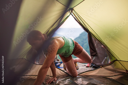 A young woman sets up sleeping bags inside a tent overlooking a gorge on a cliff in Tennessee photo