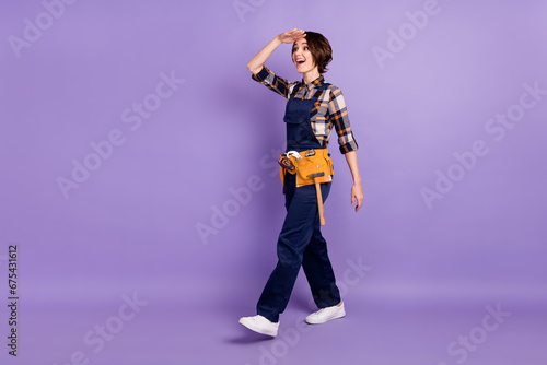 Full size profile side photo of young woman happy smile repairer go walk look ahead isolated over violet color background