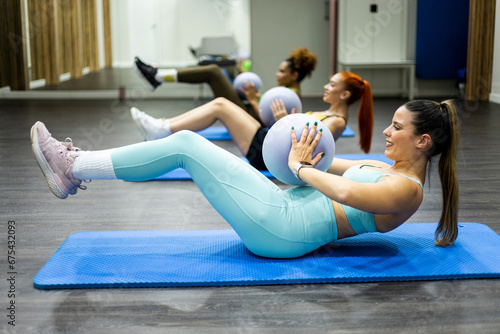 A group of 3 young women of different ethnicities are performing an abs class lying on the floor with the help of a small ball. Concept of abs classes. Take out the six-pack. Strengthen the abdomen.