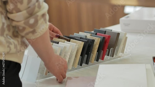 A woman with a beautiful manicure chooses a stone countertop for the kitchen in a furniture store, touches it with her hands and examines samples of materials