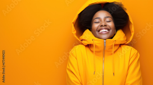 African american young smiling woman in yellow waterproof hood raincoat isolated on pastel yellow background studio portrait. Outdoors lifestyle fall weather season concept. © PaulShlykov