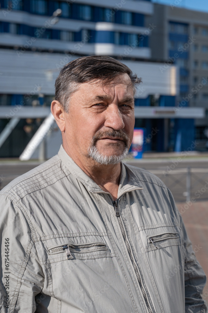 Portrait of a gray-haired 70-year-old man with a beard and mustache. A confident, serious man against the background of a business center looks into the camera Portrait of a gray-haired 70-year-old man with a beard and mustache. A confident, serious man against the background of a business center looks into the camera
