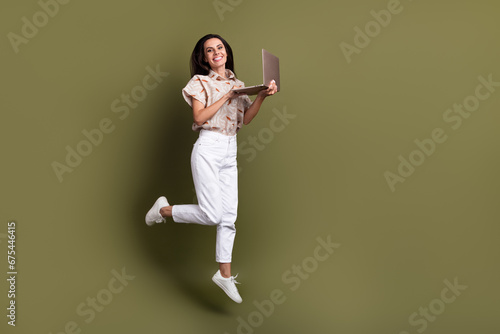Full length photo of overjoyed jumping trampoline funny woman freelance content manager using netbook isolated on khaki color background