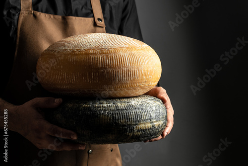 Fototapeta Naklejka Na Ścianę i Meble -  craftsmanship hands have a typical Italian cheese. French tomme cheese in the hands of a cheesemaker on dark background. Long banner format