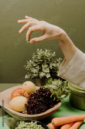 A woman's hand holding a pea in front of a green background