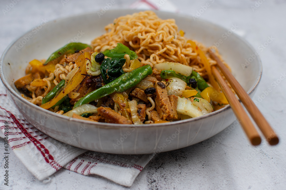 Plant based noodle bowl consisting of ramen, seitan and vegetables. White bowl, chopsticks and white table. Plant based noodle bowl consisting of ramen, seitan and vegetables. White bowl, chopsticks and white table.