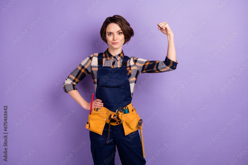Photo of young woman builder show hand biceps power strong hero isolated over purple color background Photo of young woman builder show hand biceps power strong hero isolated over purple color background