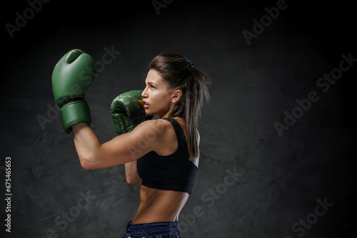 Fit woman boxer in athletic wear, displaying her punch techniques with gloves on, set against a moody background © Fxquadro