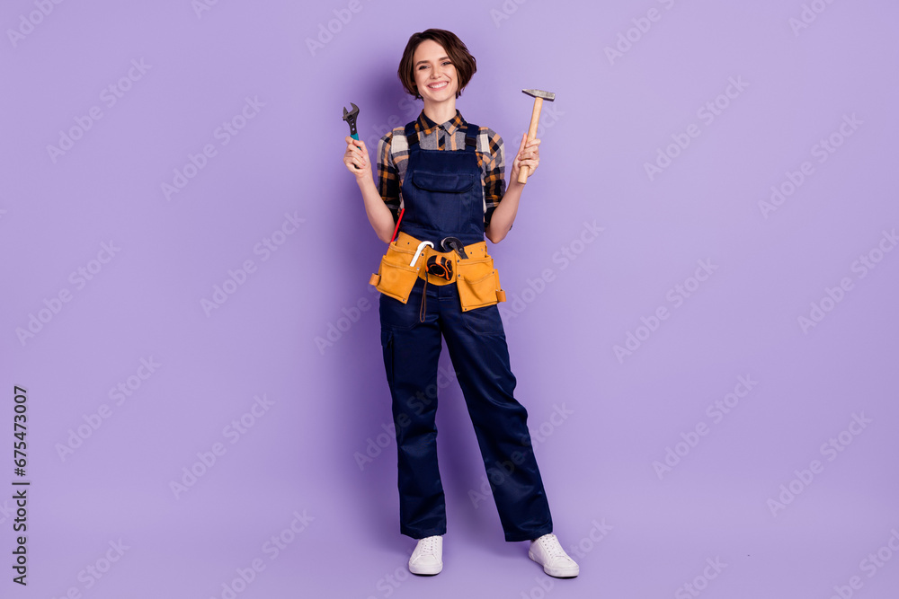 Full body photo of young woman happy smile repairer builder hold tools hammer wrench isolated over violet color background Full body photo of young woman happy smile repairer builder hold tools hammer wrench isolated over violet color background