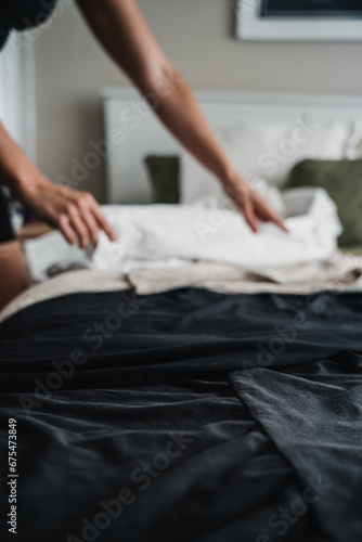 Neutral coloured clothes laid out on a bed with a woman folding them in the background.