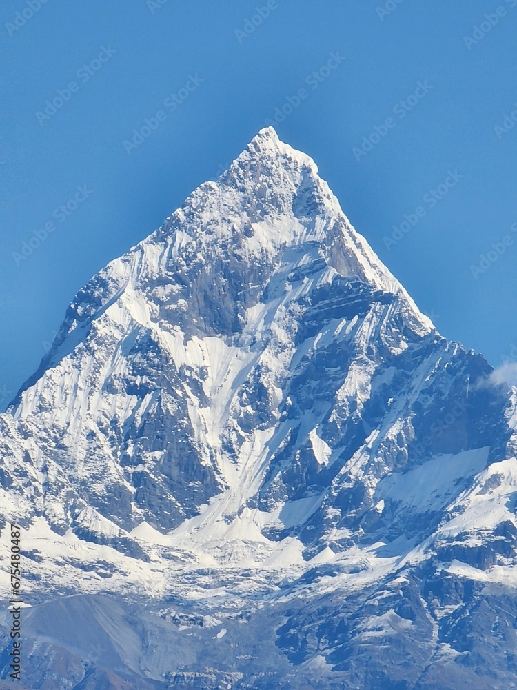 Incredible aerial shot of a majestic snow-covered mountain peak against a bright blue sky