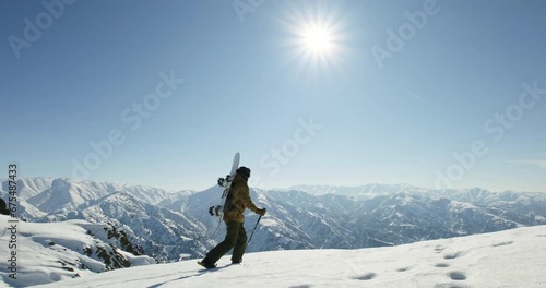 Man with snowboard hiking up to the mountain top. Extreme off-trail freeriding, winter sports vacations, outdoor winter activities and adventure photo