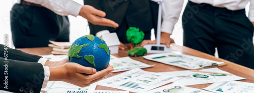 Businessman hand holding paper Earth with business people on meeting in office, planning and implementing eco-friendly ideal for corporate policy to reduce CO2 emission and save earth. Trailblazing photo