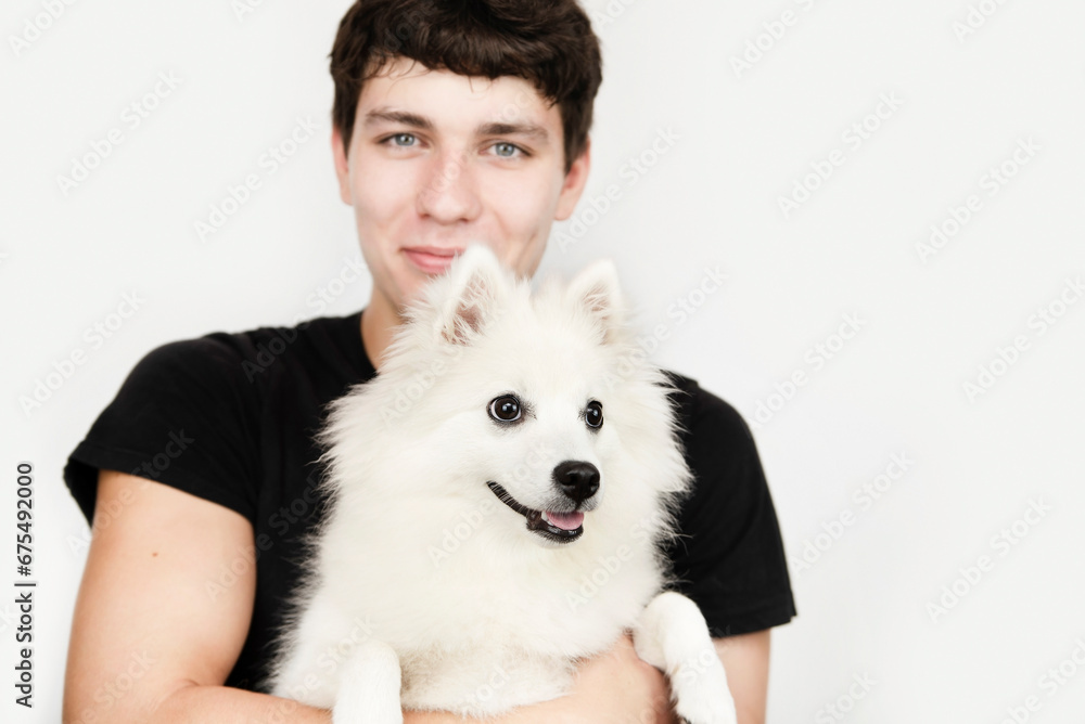 An adult spitz dog in the arms of its owner, a young guy, the guy is very happy to communicate with the dog and smiles, the concept of zootherapy An adult spitz dog in the arms of its owner, a young guy, the guy is very happy to communicate with the dog and smiles, the concept of zootherapy