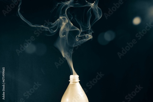 Plastic bottle with its lid off emits a plume of smoke into the air on the dark background photo
