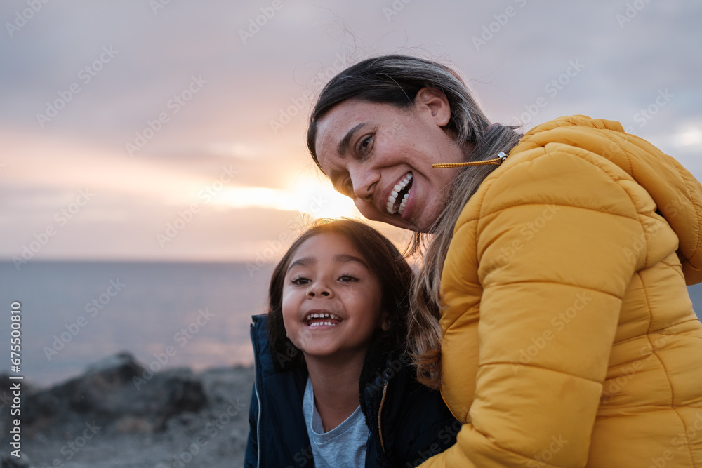 Photo of mother and daughter wrapped up in a sunset by the sea. Concept: lifestyle, together, love