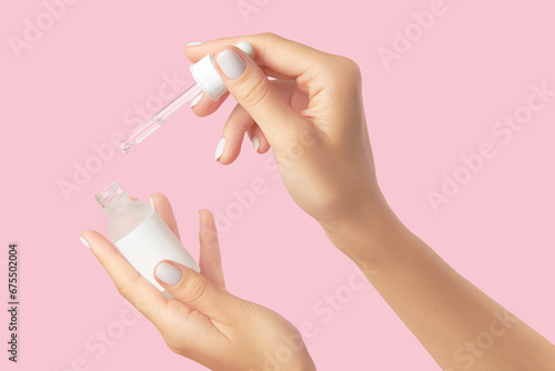 Womans hands holding dropper on pastel pink background. Self care beauty treatment concept © Darya Lavinskaya