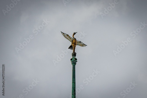 Figurine of a bird perched atop a wooden post, its wings spread wide open in a majestic display