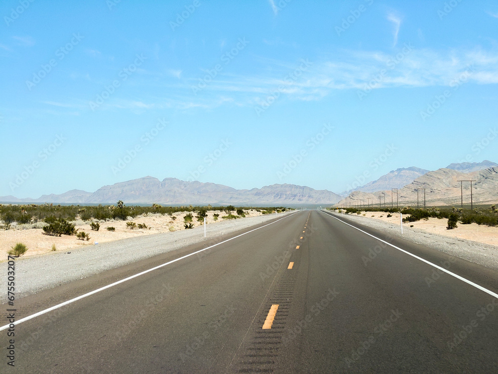 endless road in the desert, route 93, image shows a endless asphalt road in the Nevada desert, surrounded by untouched land and sand, with distant mountain views and rocks, taken october 2023