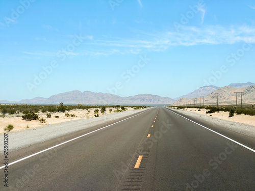 endless road in the desert, route 93, image shows a endless asphalt road in the Nevada desert, surrounded by untouched land and sand, with distant mountain views and rocks, taken october 2023 © J.Woolley