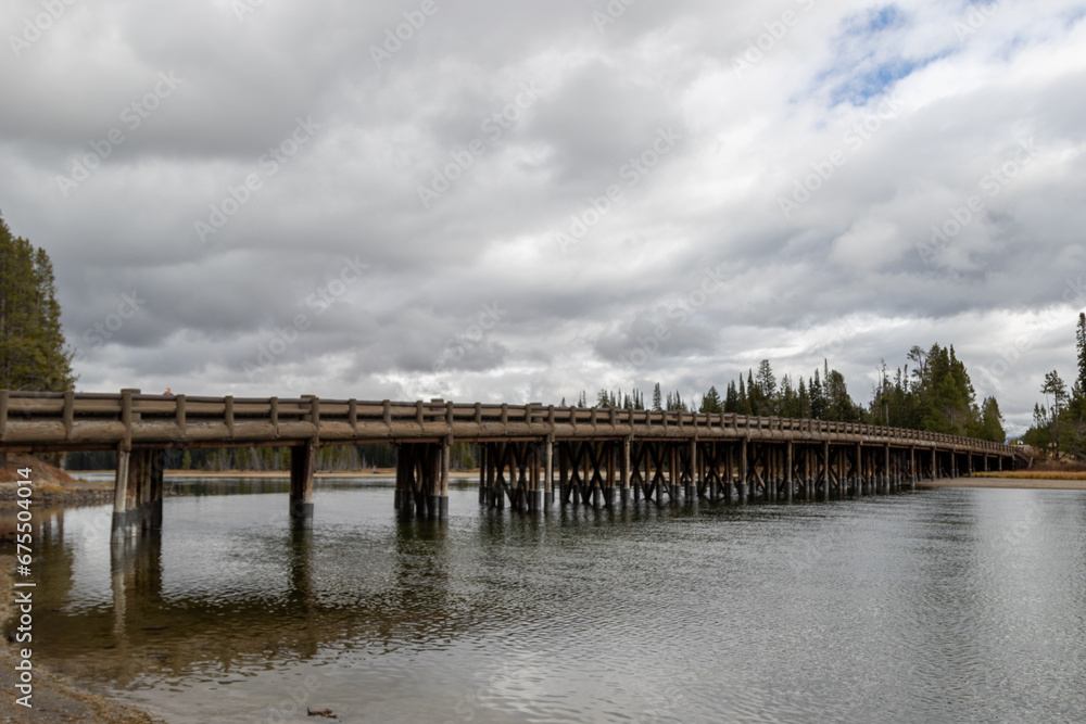A view of the Fishing bridge on Yellowstone lake near the Pelican creek nature trailhead, Image shows a ground view of the bridge with flowing water underneath with dark grey clouds overhead