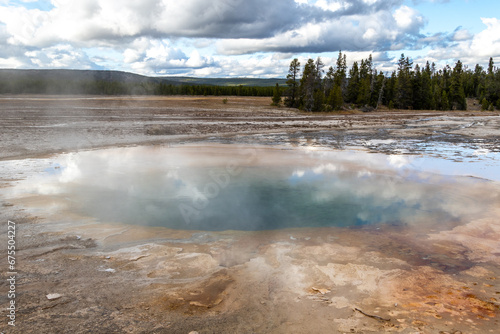 View of the multicolored Opal Pool in Yellowstone National Park with blue cloudy skies on a cold winters day days before the park closes for the season