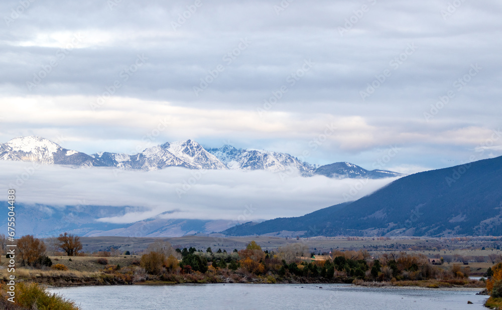 River view with low level cloud and snow covered mountains on the outskirts of Yellowstone national park on a cold autumn's day
