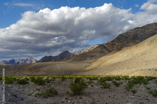 Death Valley national Park in California. Eroded mountains, creosote bush and big clouds.