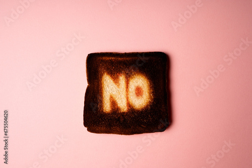 burnt slice of white bread toast with the word No on it on pink background passionate ardent disagreement. poster creative rejection concept composition 