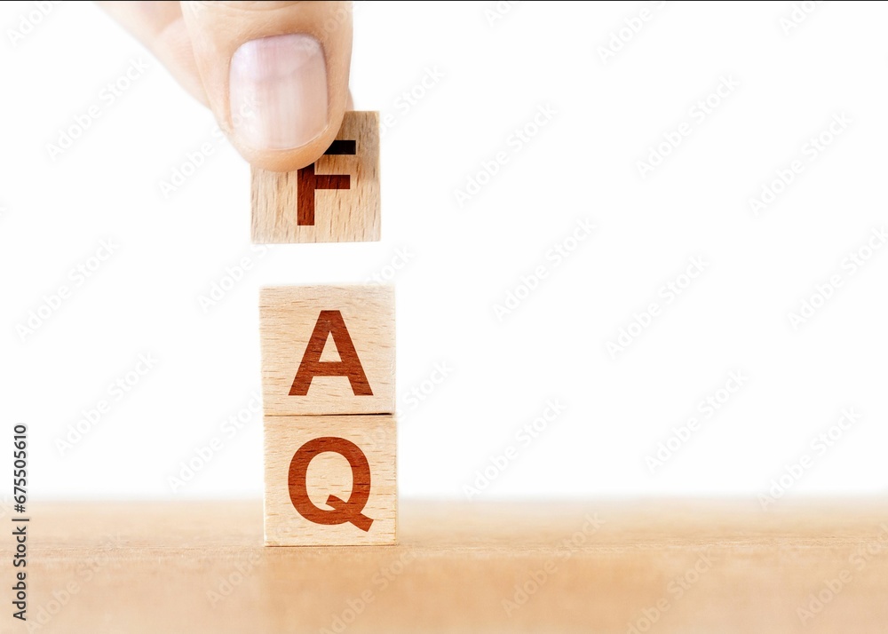 Person attempting to stack a wooden block on top of an FAQ document Person attempting to stack a wooden block on top of an FAQ document