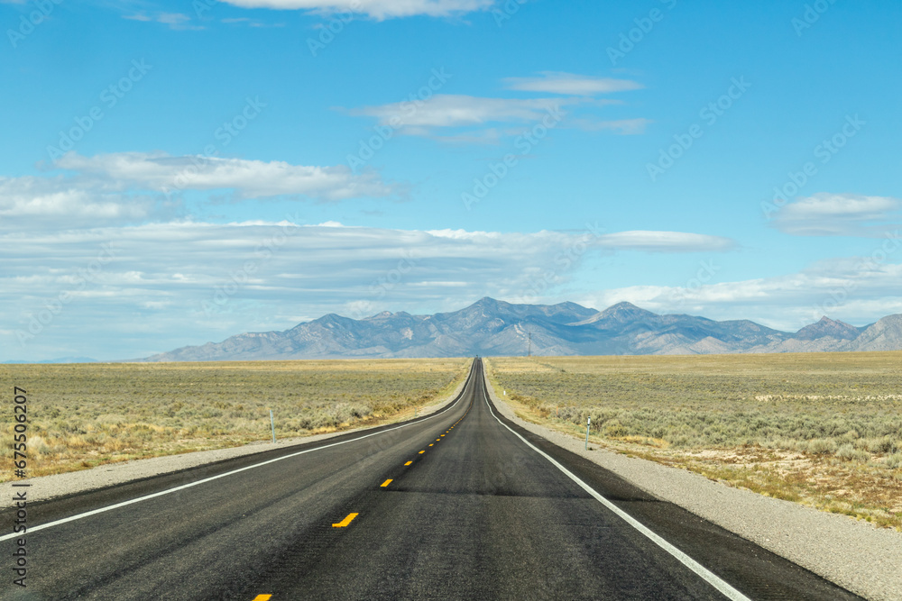 endless road in the desert, route 93, image shows a endless asphalt road in the Nevada desert, surrounded by untouched land and sand, with distant mountain views and rocks, taken october 2023