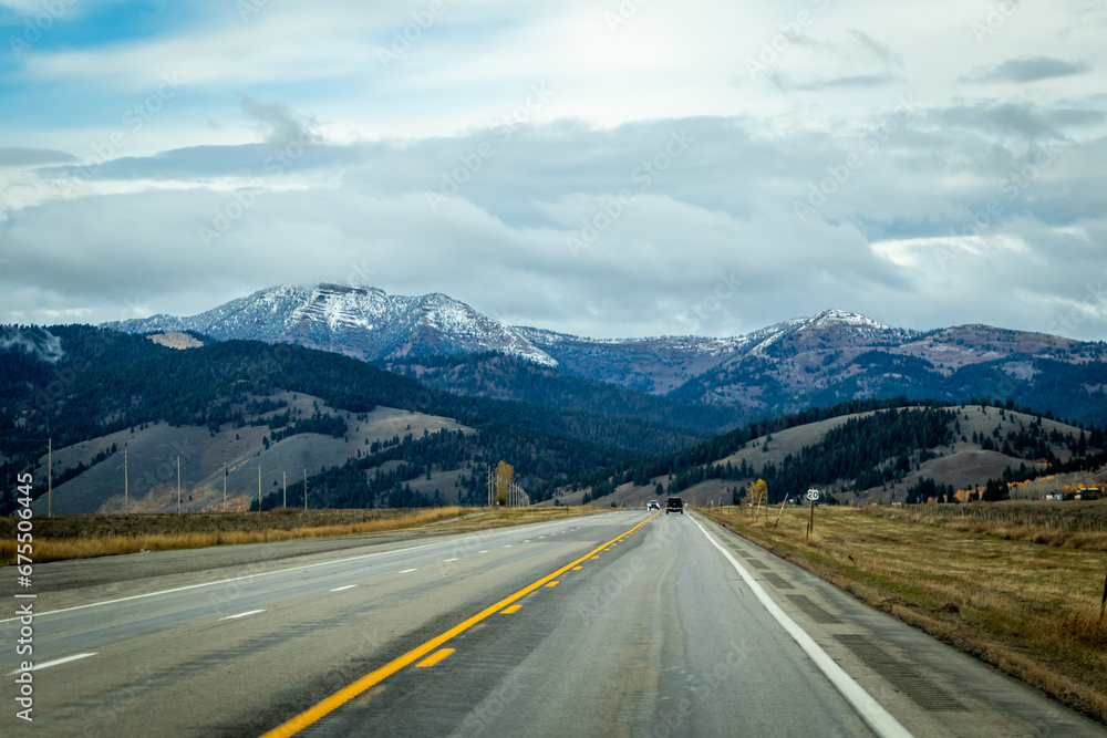 road to the mountains, image shows a endless road heading towards the mountains with a few vehicles on the road and a mountain range in the distant, with grey clouds above, taken october 2023