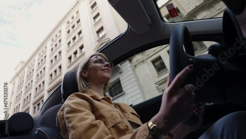 Confident young adult Caucasian woman enjoys driving an electric convertible vehicle in city, embodying freedom and eco-friendly living.  Eco-conscious woman enjoys a ride in sustainable electric auto photo