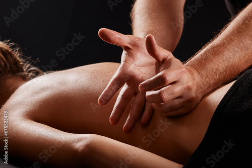 handsome male masseur giving massage to girl on black background  concept of therapeutic relaxing massage