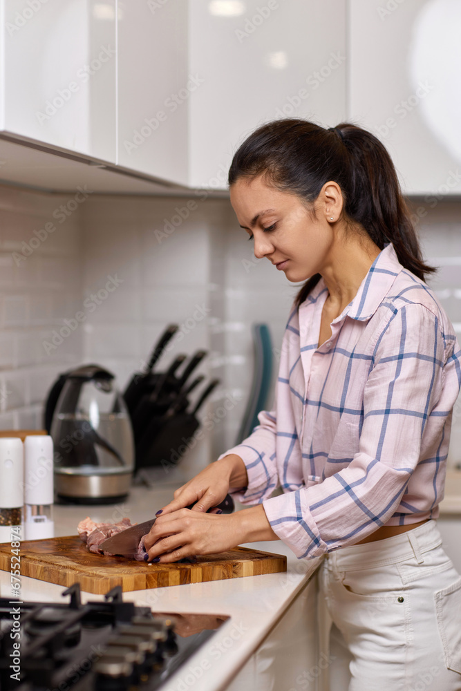 Woman is cooking piece of beef on cutting board in home kitchen Woman is cooking piece of beef on cutting board in home kitchen